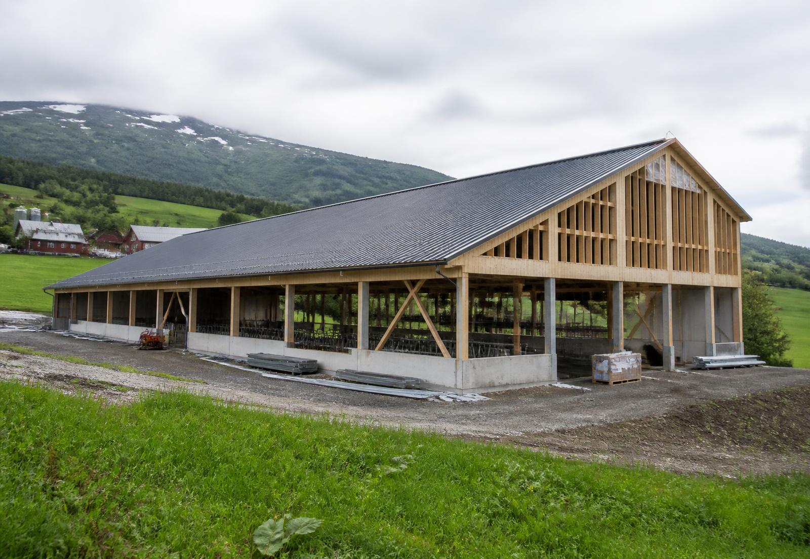 Nytt landbruksbygg under oppføring med reisverk i tre og betongvegger på ein norsk gard